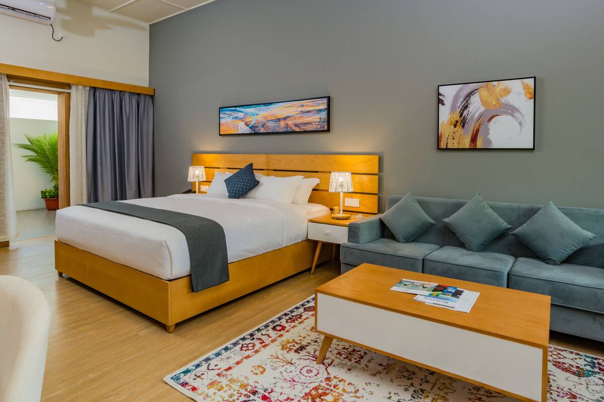 A hotel room with a bed, a sofa, a coffee table, and two paintings on the wall.