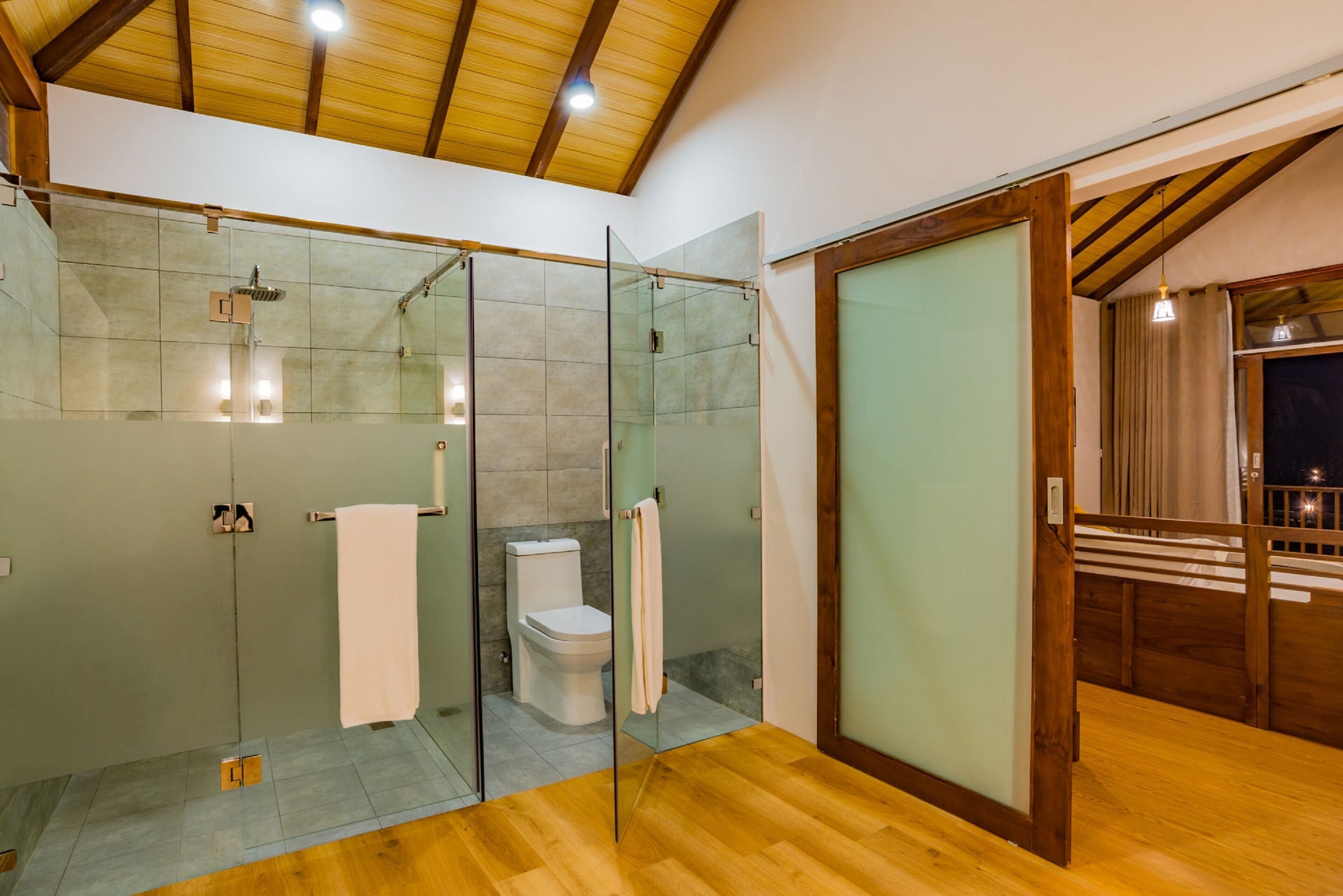 Une salle de bain moderne avec une douche à parois de verre, des toilettes et un plancher en bois.
