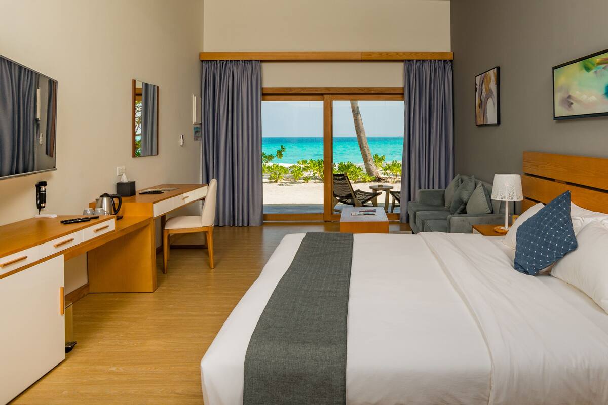 A hotel room with a bed, a desk, a chair, a table, and a view of the beach.