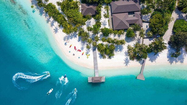An aerial view of a beach resort with a wooden pier, clear turquoise waters, and palm trees. - Fiyavalhu Resort Maldives (Mandhoo)