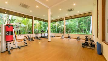 A spacious gym with various exercise equipment, large windows offering a view of lush greenery.