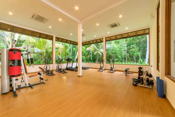 Un gimnasio espacioso con diversos equipos de ejercicio y grandes ventanales que ofrecen vistas a exuberante follaje.