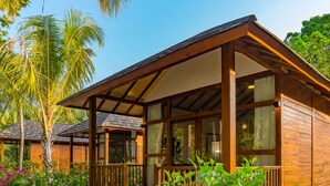A wooden bungalow with a porch, large windows, and a view of palm trees and greenery. - Fiyavalhu Resort Maldives (Mandhoo)