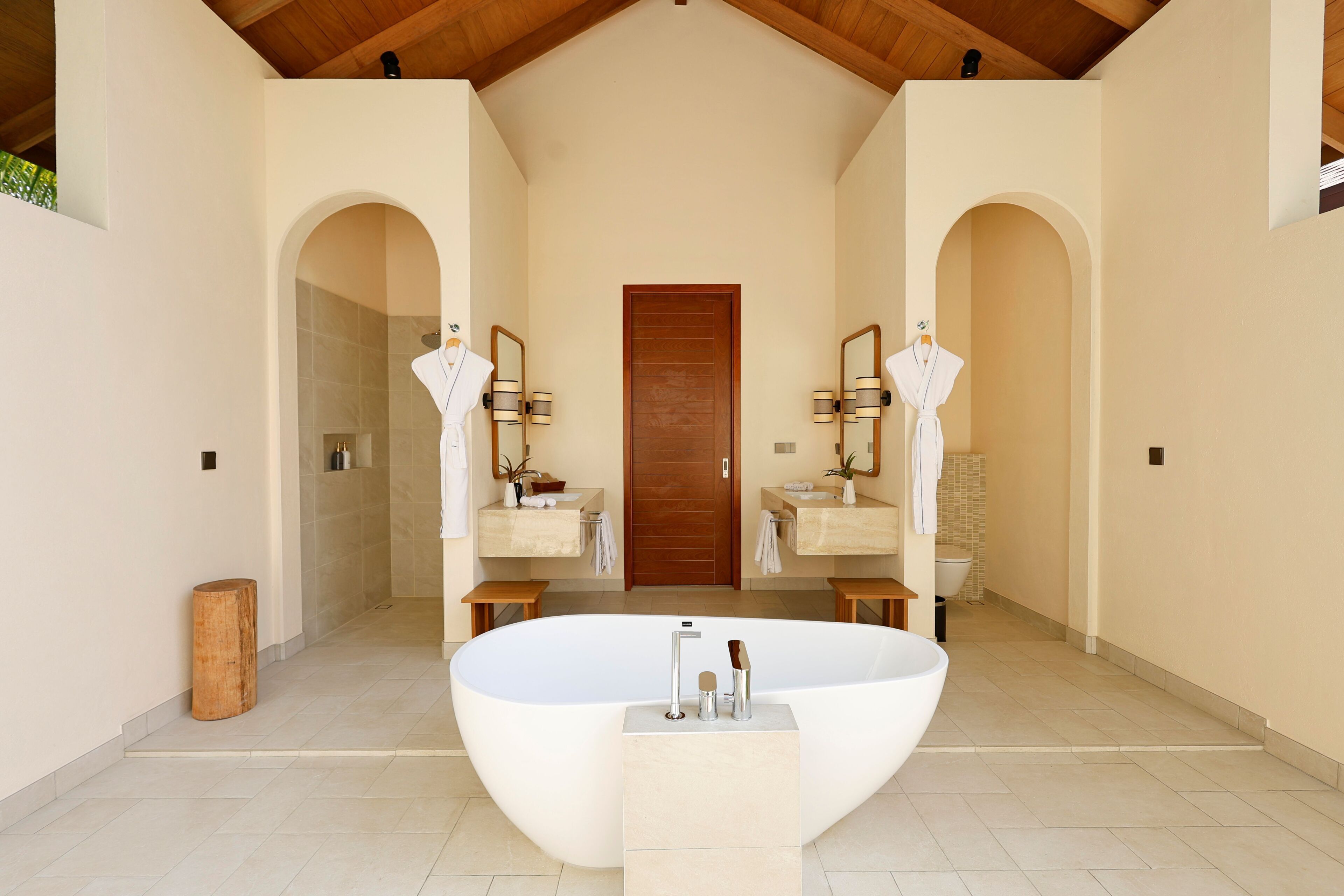 A spacious bathroom with a freestanding bathtub, two vanity mirrors, and a wooden door.