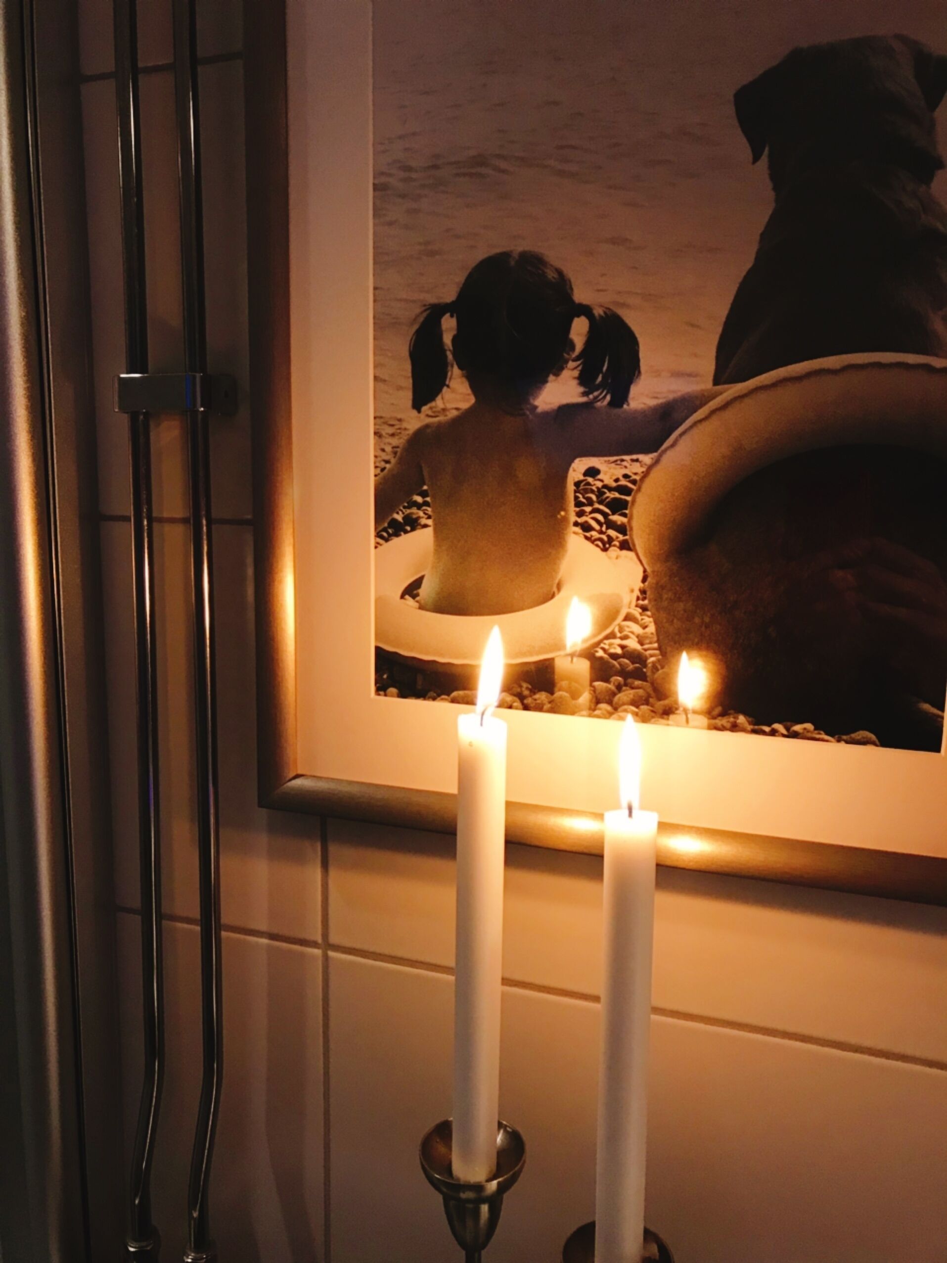 A framed picture of a beach scene with two candles in front of it.