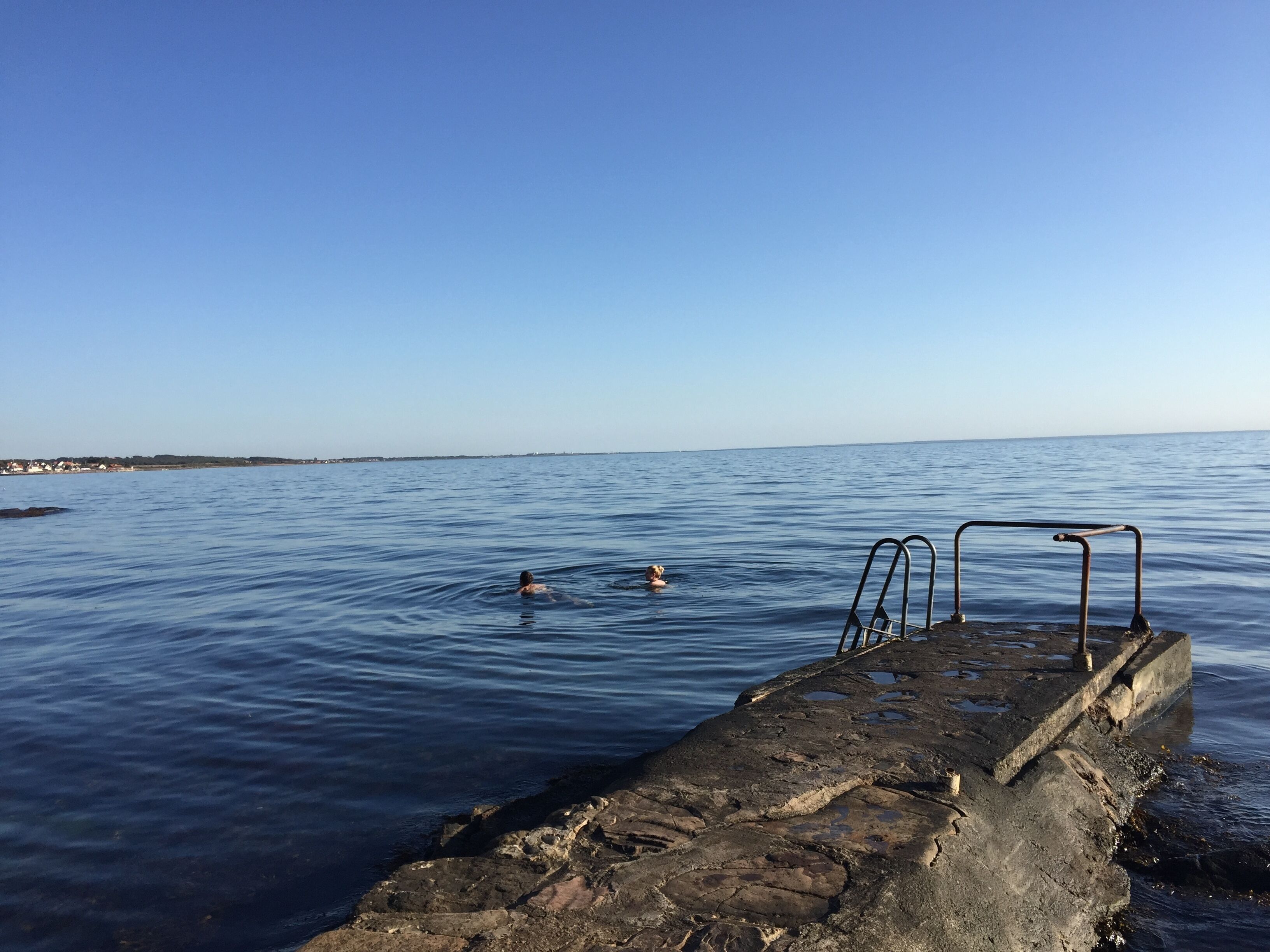 A rocky pier extending into calm waters with a metal ladder.