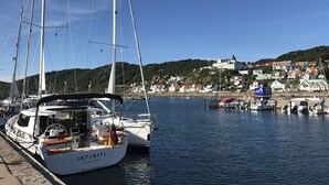 A marina with several sailboats docked, a white building with a green roof in the background, and a clear blue sky. - Villa Lindell (Hoganas)