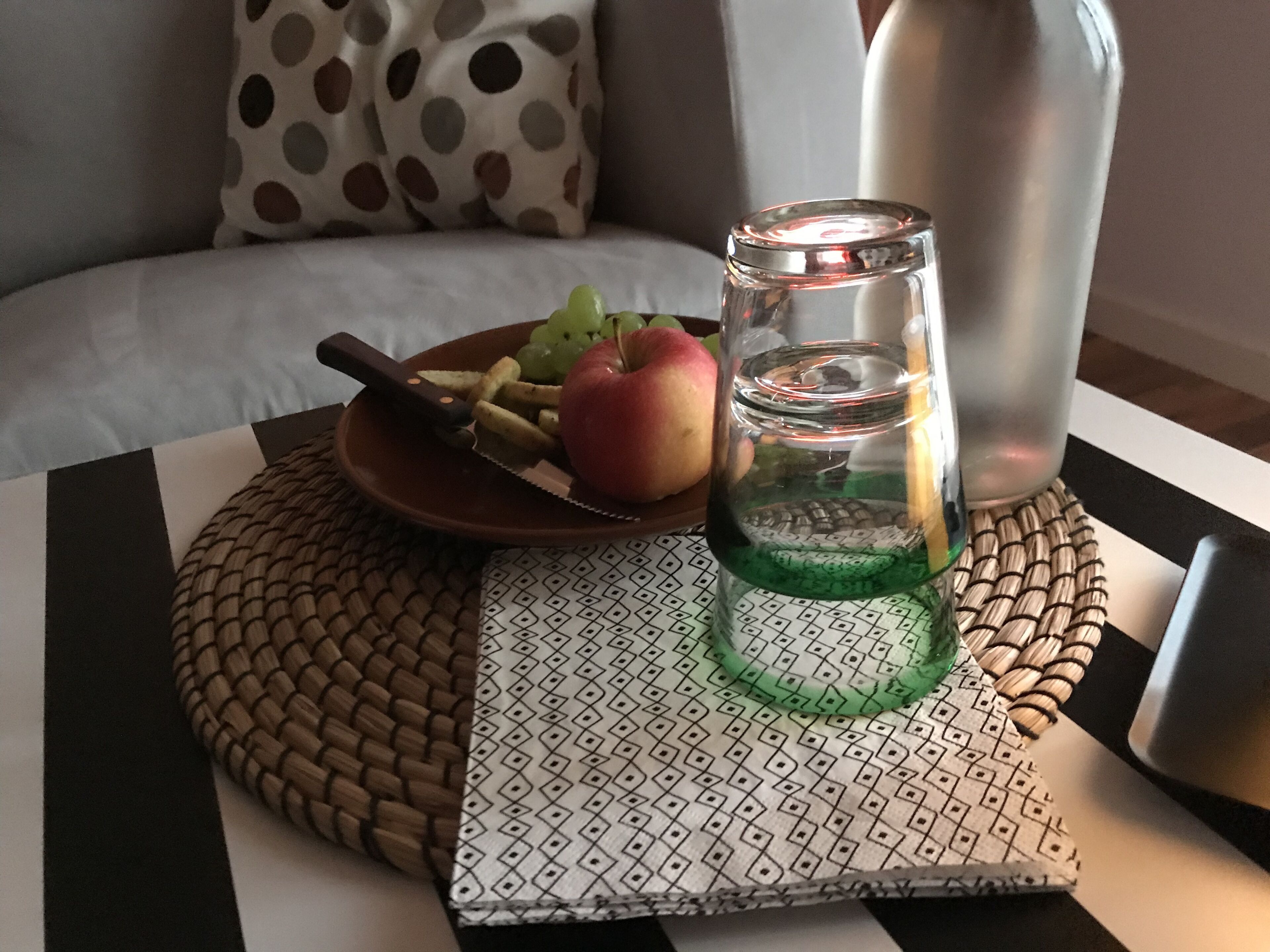 Ruokapöytä, jonka päällä on lautanen täynnä ruokaa, veitsi, vihreää sisältöä sisältävä lasipurkki ja vesipullo.