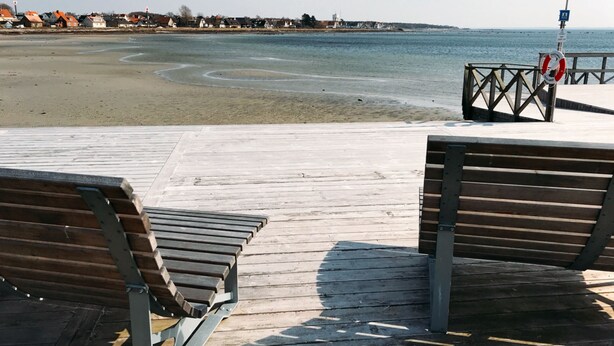 A wooden pier with benches overlooking a beach and a calm sea. - Villa Lindell (Hoganas)