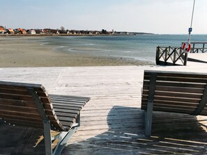 A wooden pier with benches overlooking a beach and a calm sea.