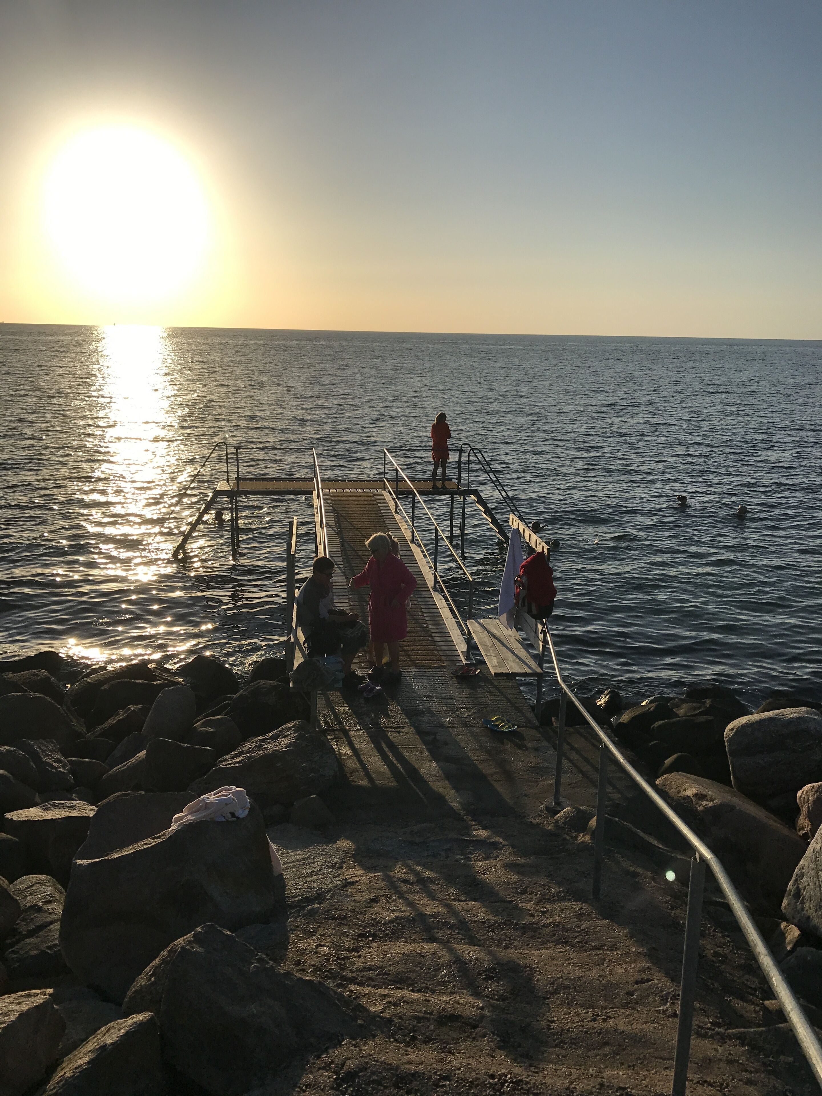 Un muelle se adentra en aguas tranquilas, con un atardecer al fondo.