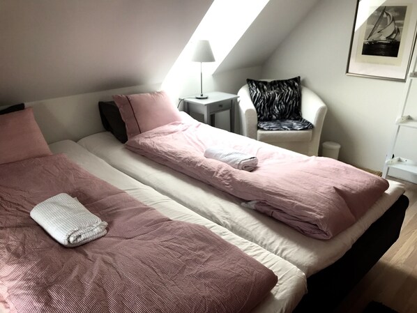 A bedroom with two beds, a small table, a chair, and a framed picture on the wall.