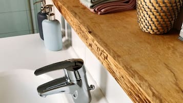 A bathroom with a wooden vanity, a white sink, a modern faucet, and a soap dish.