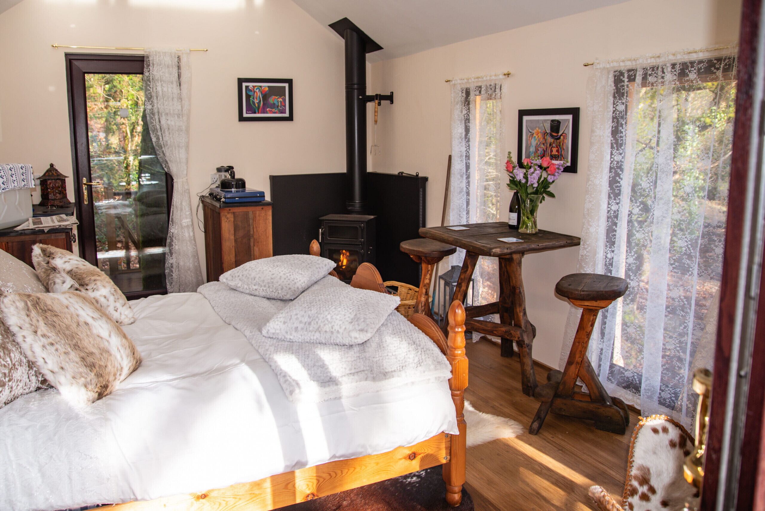 A bedroom with a bed, a wooden table, a chair, a fireplace, and a window with curtains.