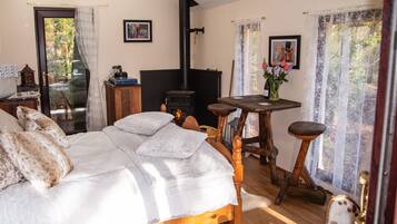 A bedroom with a bed, a wooden table, a chair, a fireplace, and a window with curtains.