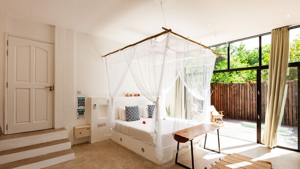 Ein Schlafzimmer mit Baldachinbett, einer Holzbank und Blick ins Freie.