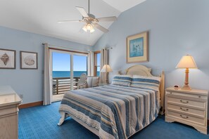 A bedroom with a bed, a nightstand, a lamp, a ceiling fan, a window, and a door leading to a balcony.