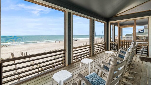 Una stanza fronte spiaggia con ampie finestre, terrazza in legno e vista sulla spiaggia.