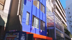 Un hôtel avec une façade bleue, une entrée bien visible et un distributeur automatique à l’extérieur.