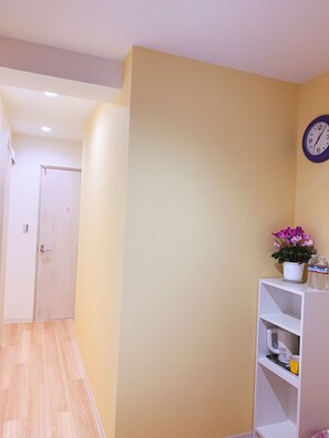 A hallway with a wooden floor, a white door, and a white shelf with a clock and a potted plant. - Akinoryokan (Tokyo)