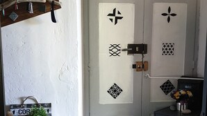 Una stanza con una porta bianca decorata con motivi neri, un tavolino con una pianta e un cartello, e un pavimento piastrellato.