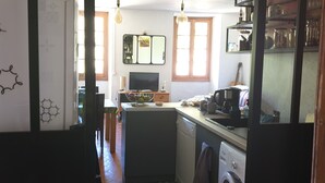 Una cucina compatta con isola centrale, lavastoviglie, lavatrice e zona pranzo con tavolo e sedie.
