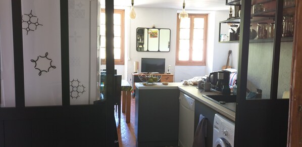 A compact kitchen with a central island, a dishwasher, a washing machine, and a dining area with a table and chairs.