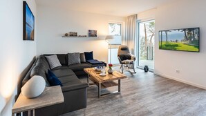 A modern living room with a grey sofa, a wooden coffee table, and a TV on the wall.