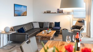 A modern living room with a sofa, coffee table, and a dining table with wine glasses.