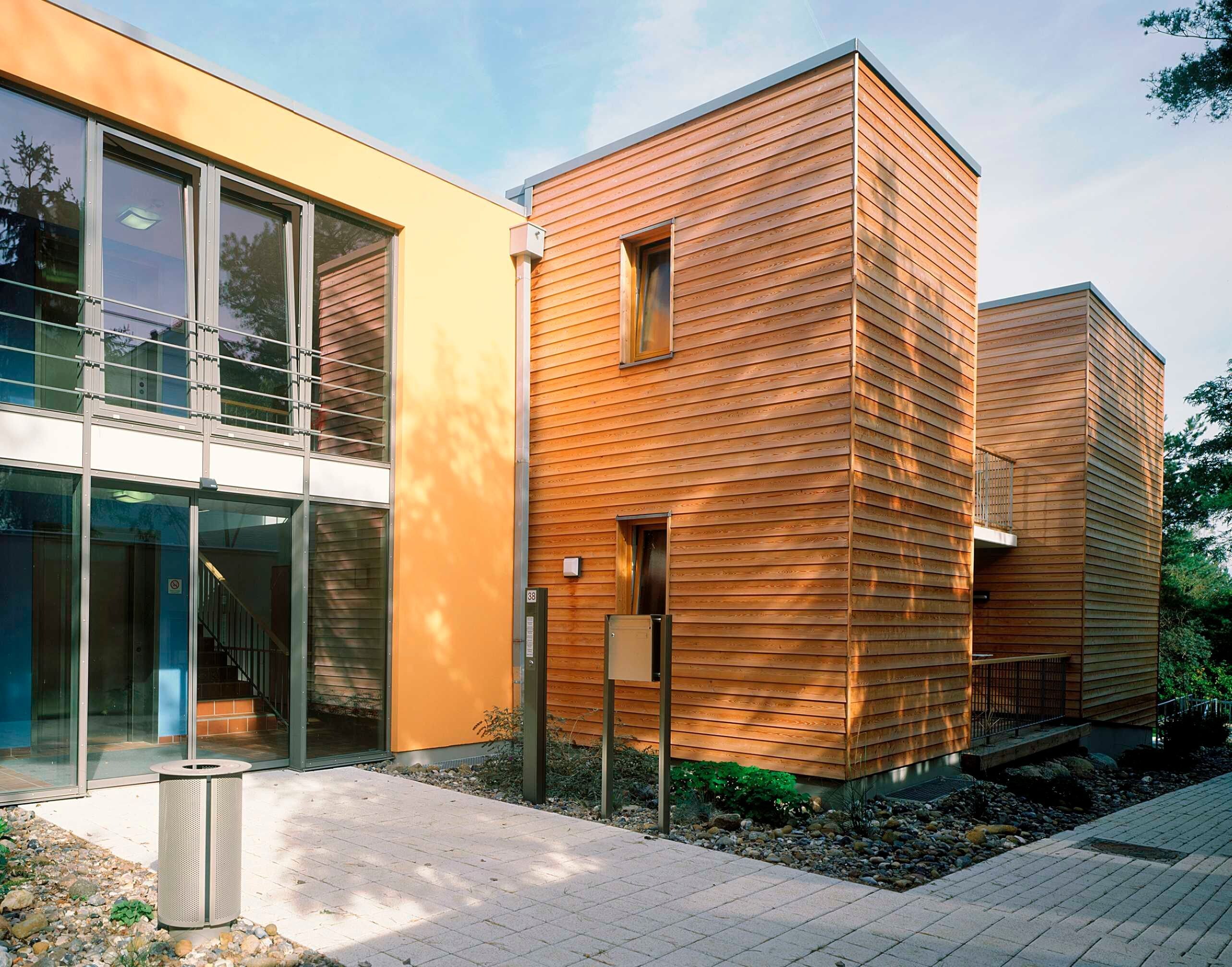A modern building with large glass windows, a wooden facade, and a paved walkway.