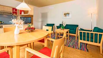 Un salon moderne avec une table à manger en bois, des chaises à coussins rouges, un canapé vert et une petite table d’appoint sur laquelle est posé un vase.