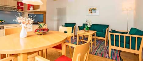Una sala moderna con una mesa de comedor de madera, sillas con cojines rojos, un sofá verde y una pequeña mesita de noche con un florero.