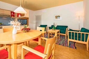 Ein modernes Wohnzimmer mit einem Holzesstisch, roten gepolsterten Stühlen, einem grünen Sofa und einem kleinen Beistelltisch mit einer Vase.