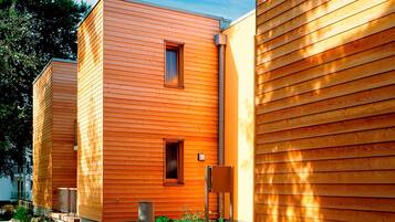 Un bâtiment moderne doté d’un revêtement extérieur en bois disposé horizontalement, de deux fenêtres apparentes et d’un petit espace extérieur agrémenté d’un chemin et de quelques plantes.