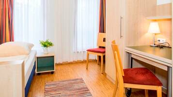Une chambre d’hôtel comprenant un lit, un bureau, une chaise, une petite table avec une lampe et une fenêtre avec des rideaux.