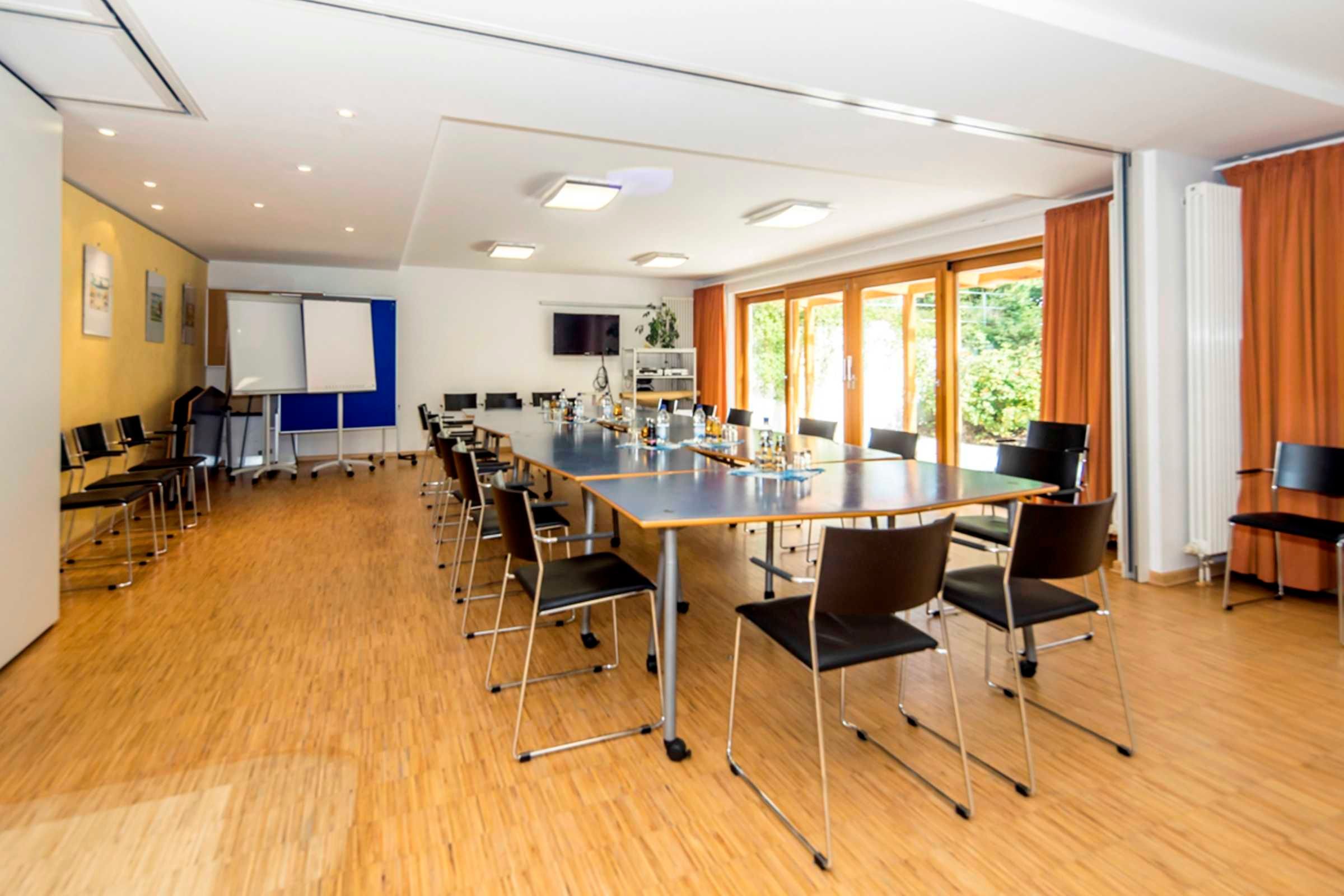 Ein Konferenzraum mit einem langen Tisch, Stühlen, einer Whiteboard-Tafel und einem Fernsehbildschirm.