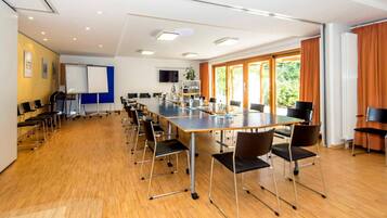 Ein Konferenzraum mit einem langen Tisch, Stühlen, einer Whiteboard-Tafel und einem Fernsehbildschirm.
