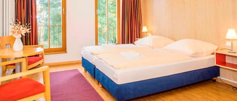 Quarto de hotel com cama, escrivaninha, cadeira e janela com cortinas.