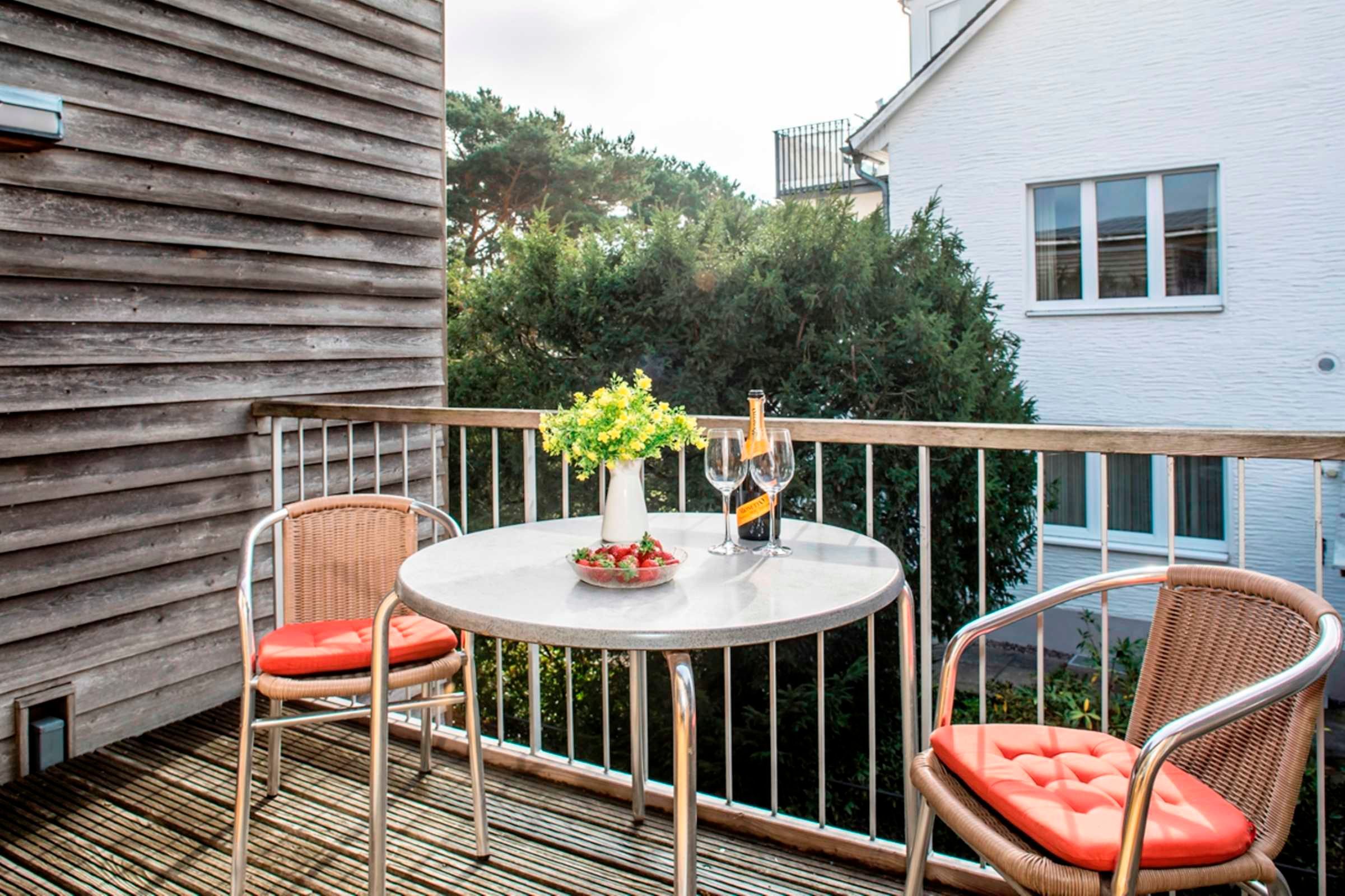 Un balcon avec deux fauteuils en osier, une petite table ronde et un vase rempli de fleurs.
