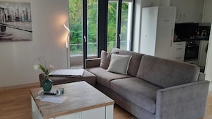 Una sala de estar moderna con un sofá, una mesa de centro, un jarrón con flores, un cuadro en la pared y vistas a la naturaleza.