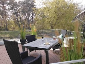Une terrasse avec une table et des chaises, donnant sur un plan d’eau et des arbres.