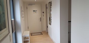 A hallway with a white door, a small bench, a mat with 'HEIMAT' on it, and a wall-mounted air conditioning unit.