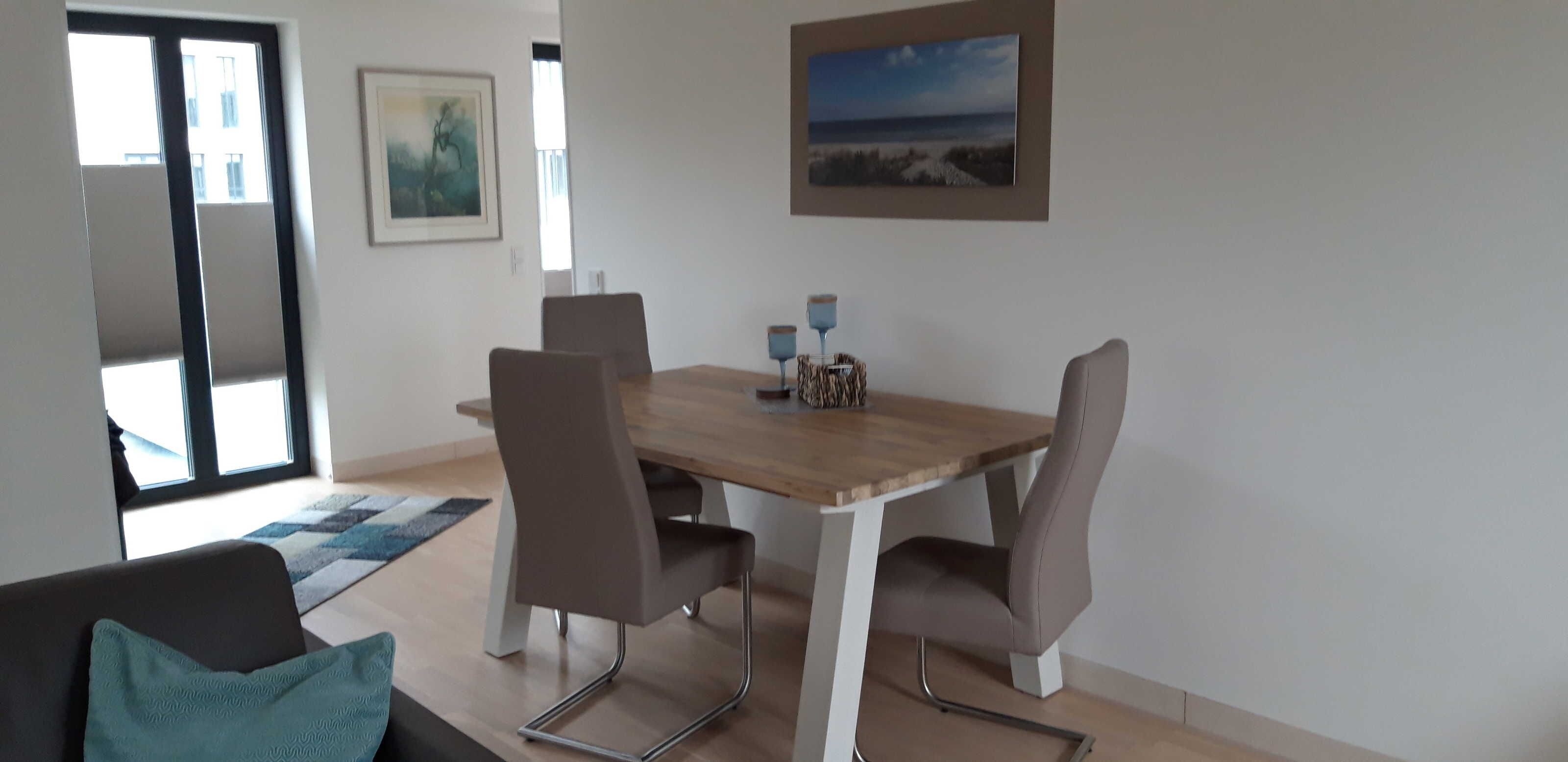 A dining area with a wooden table, four chairs, a blue rug, and two wall-mounted lamps.