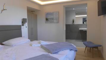 Een moderne hotelkamer met een bed, een stoel, een bureau en een badkamer zichtbaar door een glazen deur.