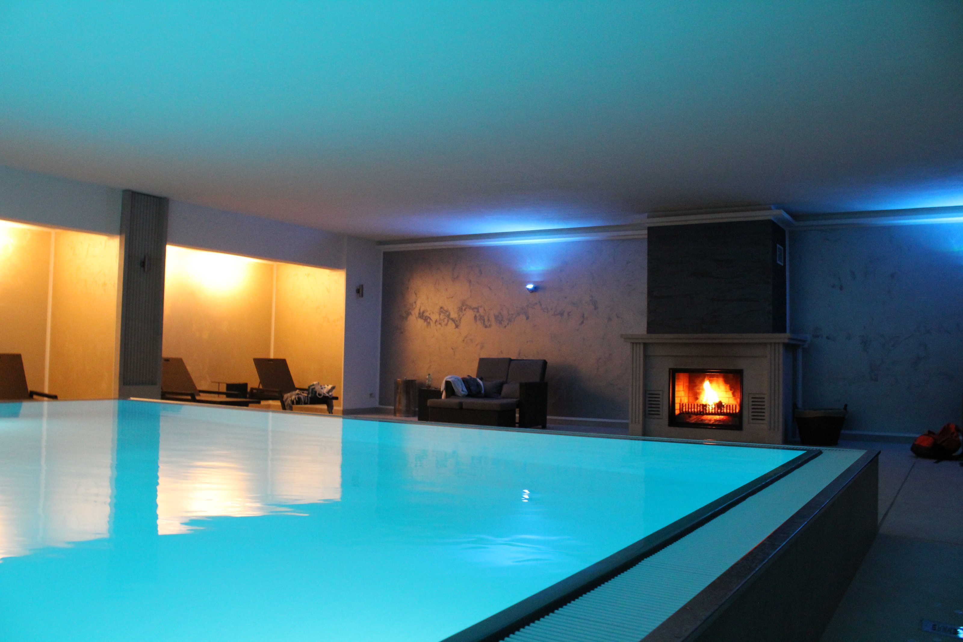 A swimming pool with lounge chairs, a fireplace, and a stone wall.
