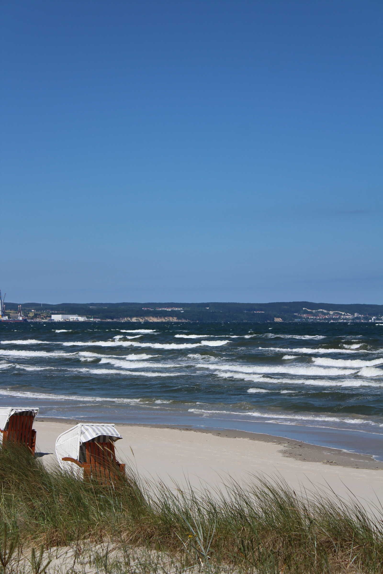 Una playa con olas, una silla y un edificio al fondo.