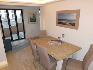A dining area with a wooden table, four chairs, two wine glasses, and a framed picture on the wall.