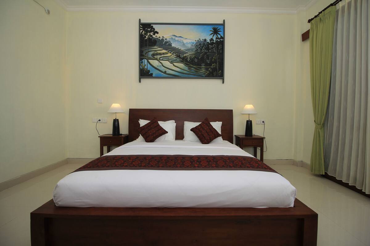 A neatly made bed with a wooden headboard, two bedside tables with lamps, and a painting above the bed.