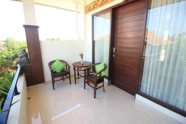 A balcony with two wooden chairs, a small table, and a statue. - Brata Cottage Bisma Ubud by Summer Stay (Ubud)