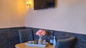A dining area with a table, chairs, a TV mounted on the wall, and decorative wall lights. - Kos - sparrow lust - sparrow lust (Koserow)